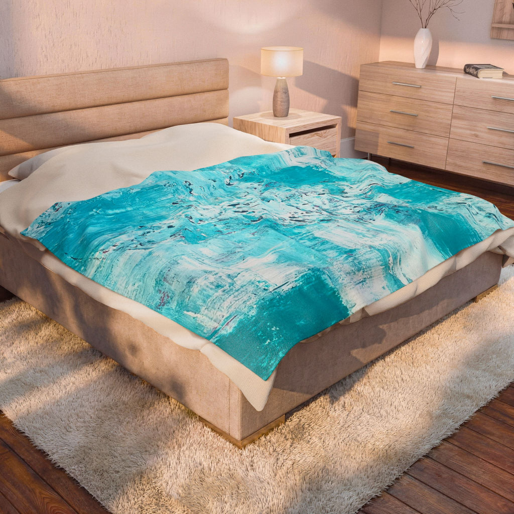 Turquoise abstract plush throw blanket on bed, partly folded over white bedding