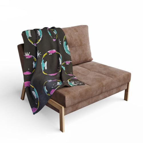 Fleece throw blanket with dark base and colorful bubble/planet pattern, draped on chair
