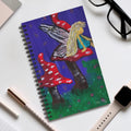Spiral journal with fairy character and red mushroom details on a colorful cover.