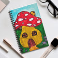 Spiral journal with red mushroom and yellow cottage illustration on a turquoise cover.