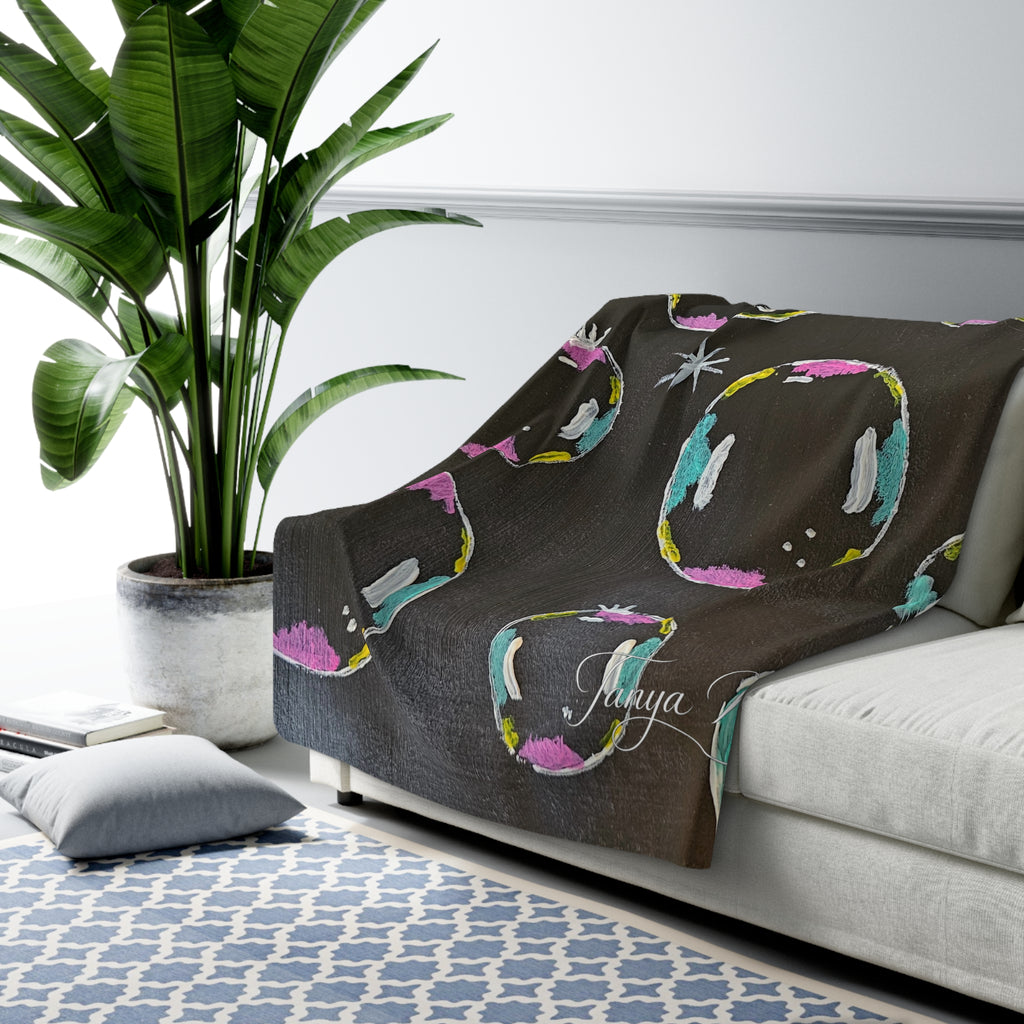 Sherpa fleece blanket on sofa, dark gray with colorful bubble circles and scattered star accents