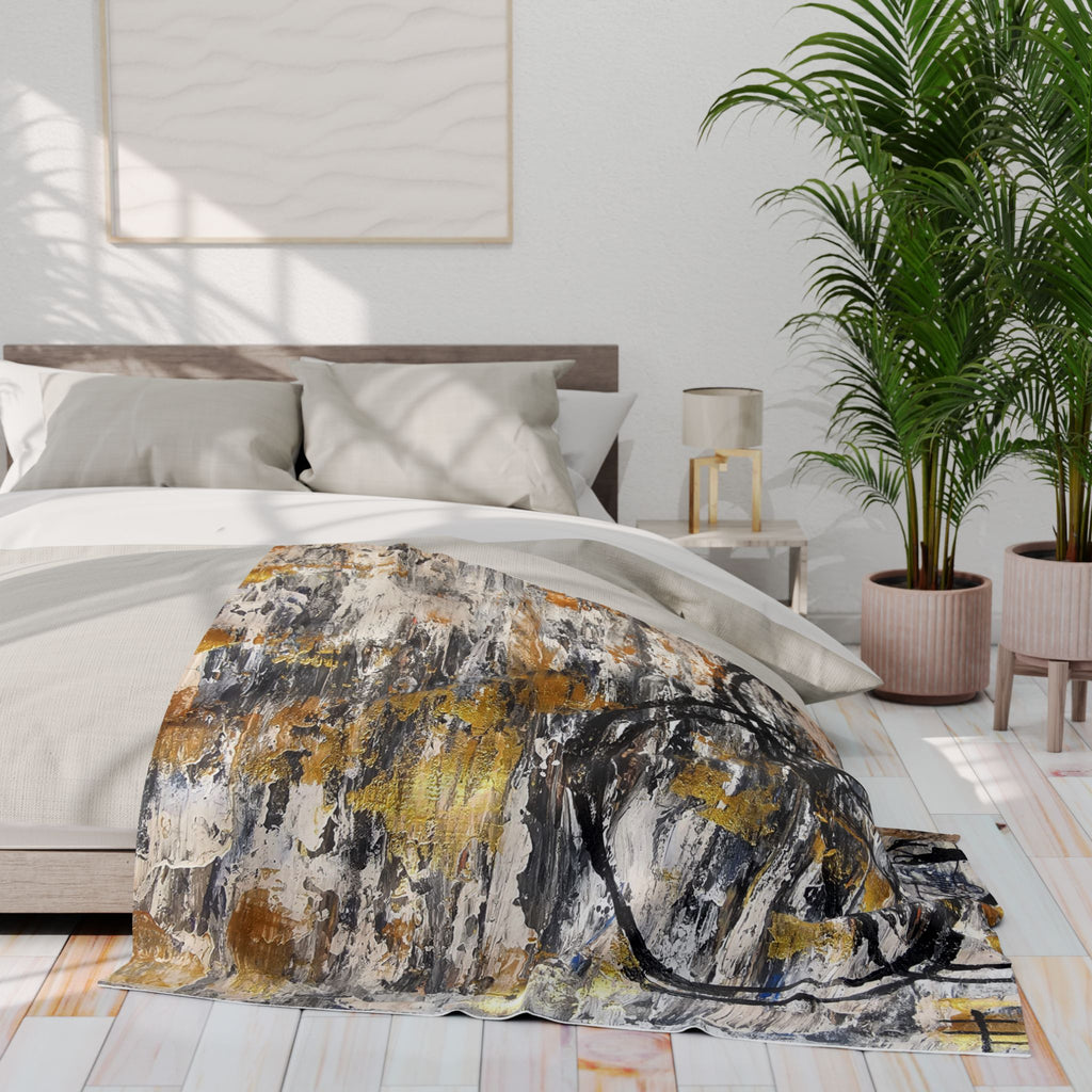 Fleece blanket with abstract gold, grey, and black swirls laid across a bed