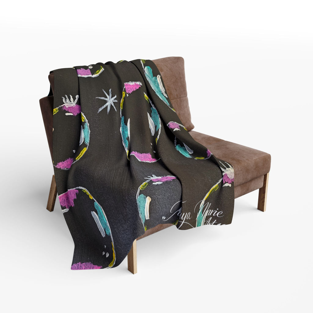 Fleece throw blanket draped over chair, dark fabric with colorful bubble/planet pattern