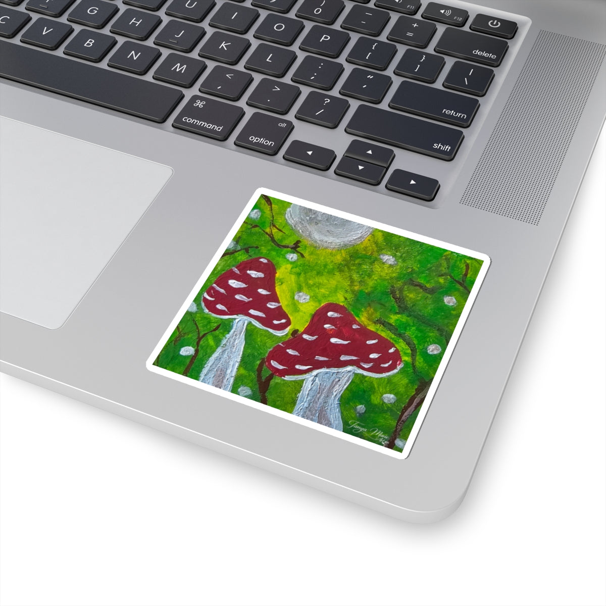 Kiss-cut sticker on a laptop, red mushrooms over green moss with white spots.