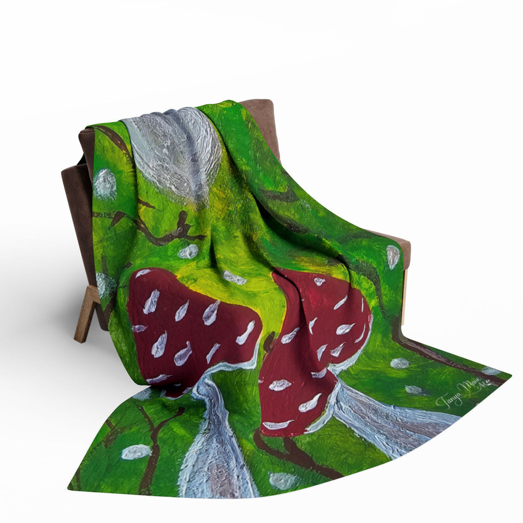 Green fleece blanket draped on chair, showing red mushrooms and gray cap art