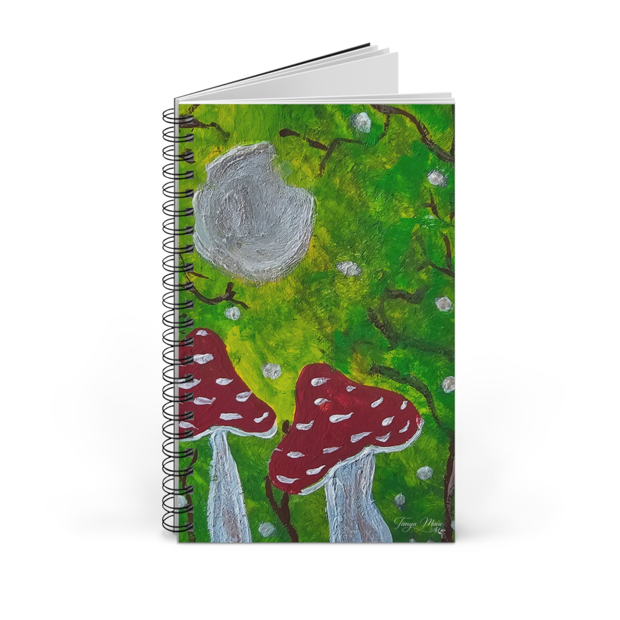 Spiral journal notebook with green illustrated cover, gray moon, red mushrooms, and stack behind
