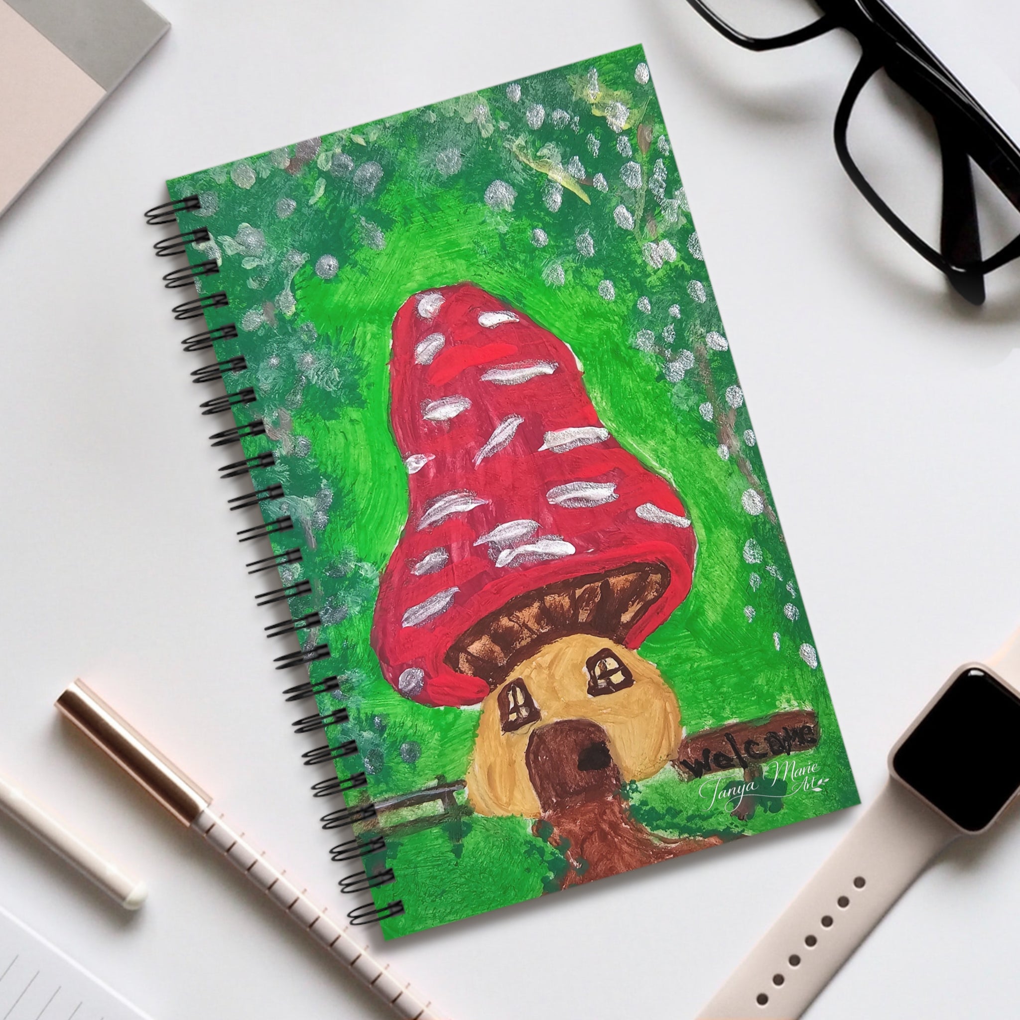 Spiral journal with green cover featuring red mushroom and fairy house illustration