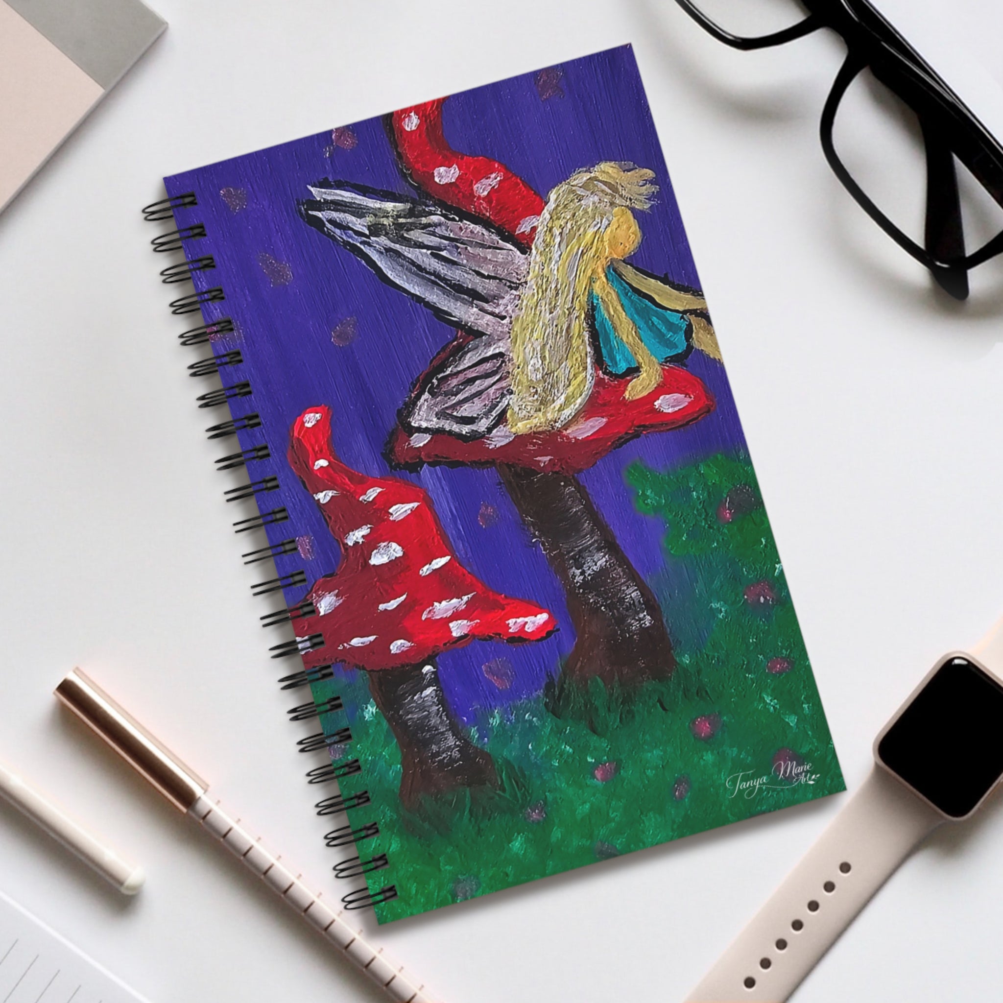 Spiral notebook with fairy and mushroom illustration on a blue cover, black coil