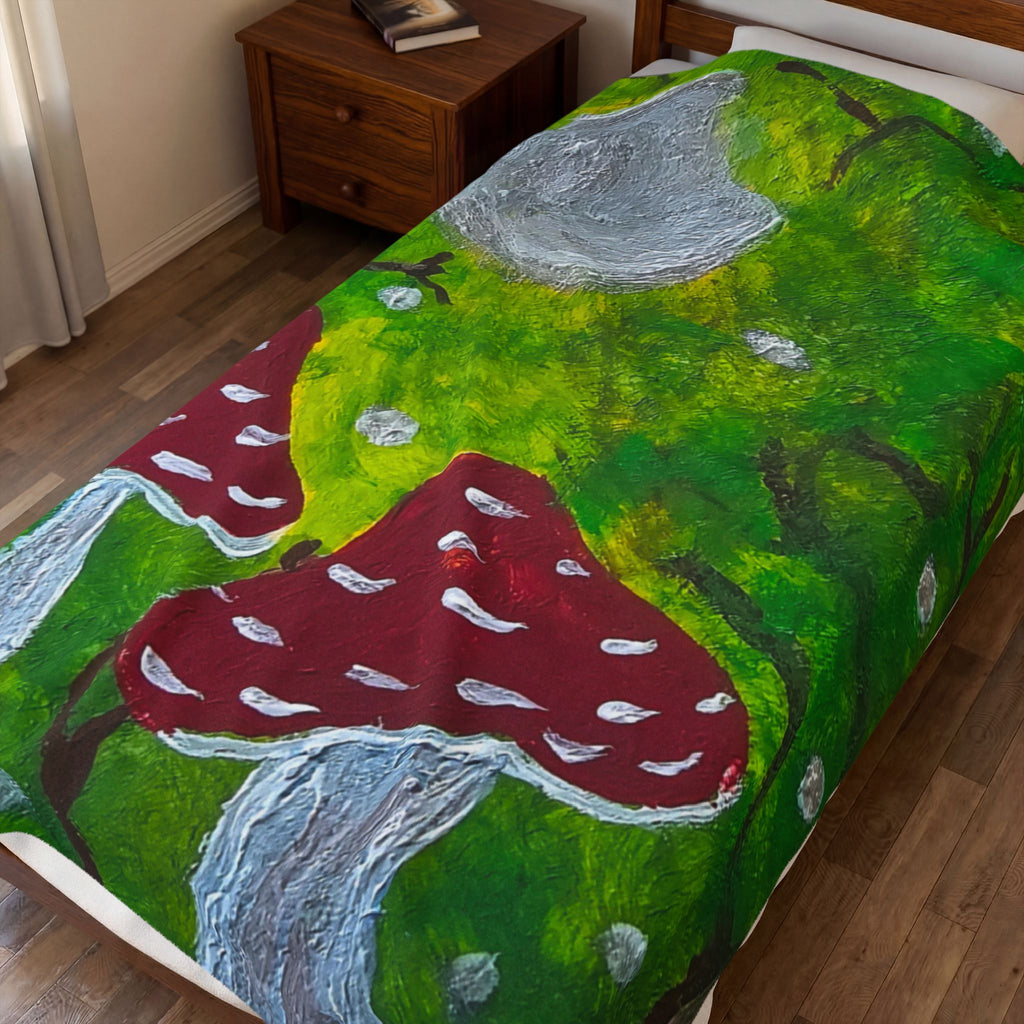 Plush velveteen blanket with green forest artwork, red mushrooms, and gray rock