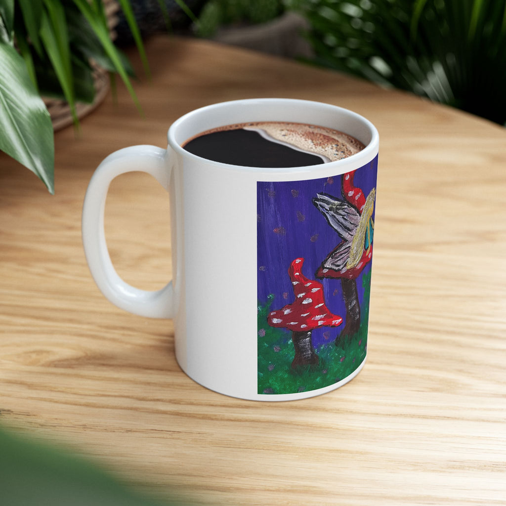 White ceramic mug filled with coffee, fairy and toadstool artwork on front
