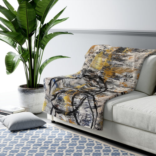 Sherpa throw blanket with abstract gold and charcoal brushstroke design over a sofa