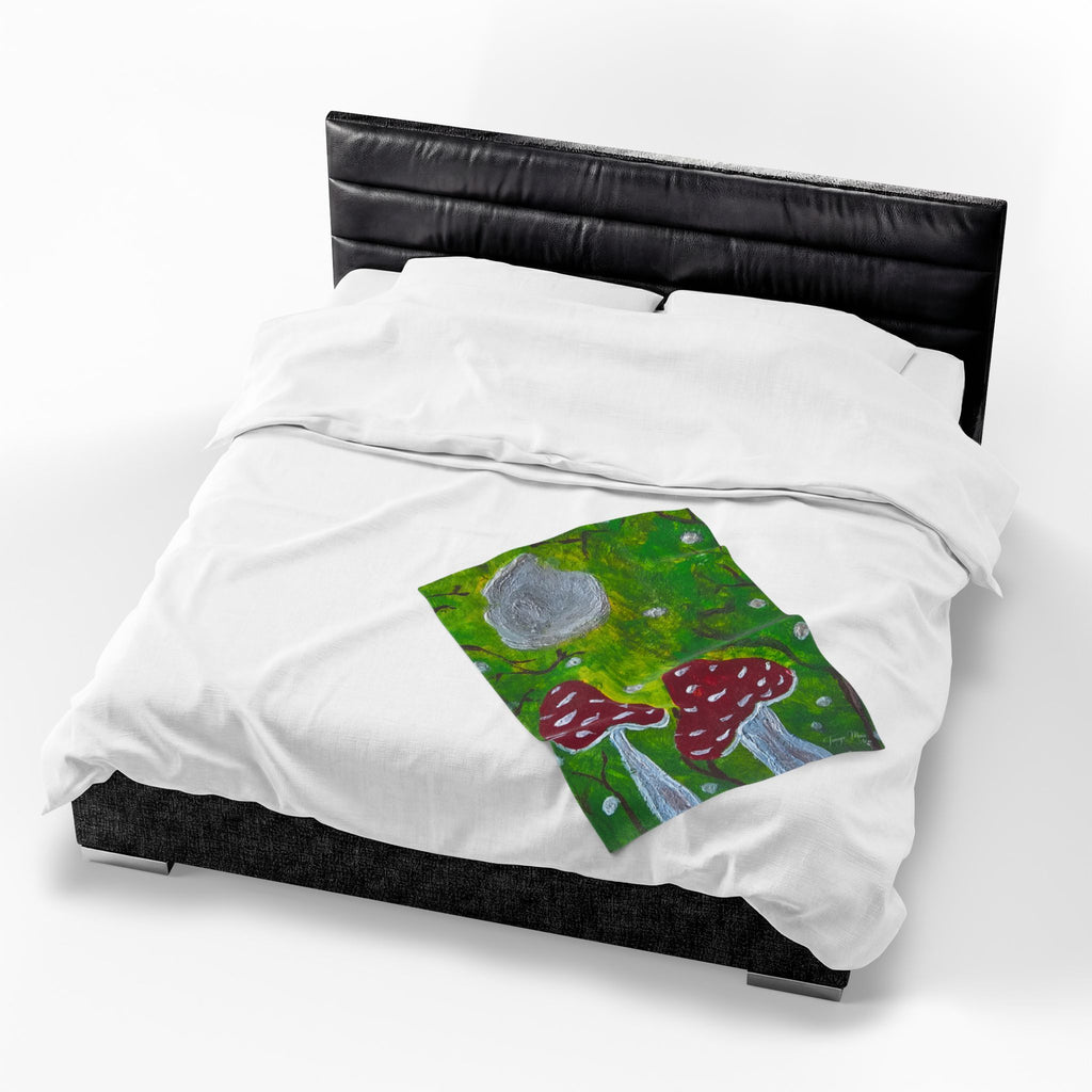 White plush blanket with green forest motif: red mushrooms and gray moon patch.