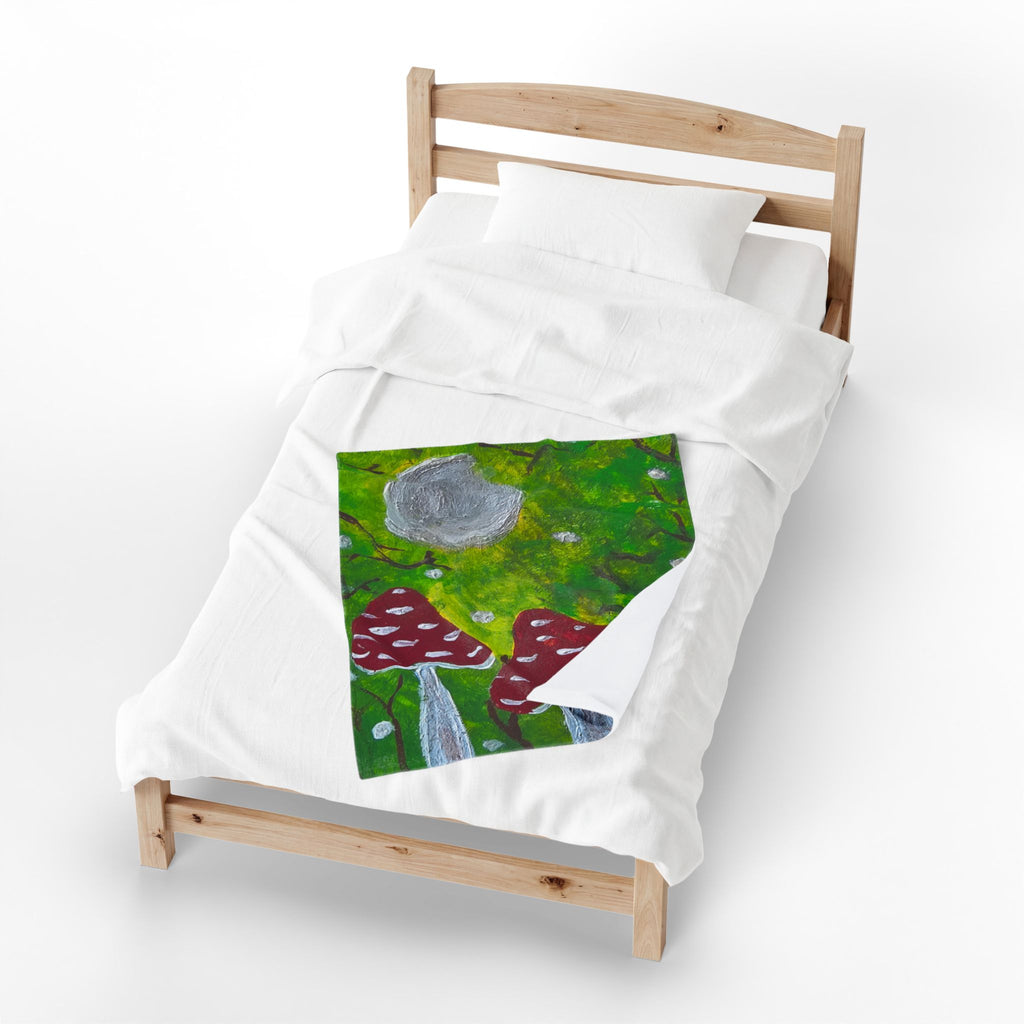 White plush blanket with stitched green forest art, red mushroom caps, gray moon.