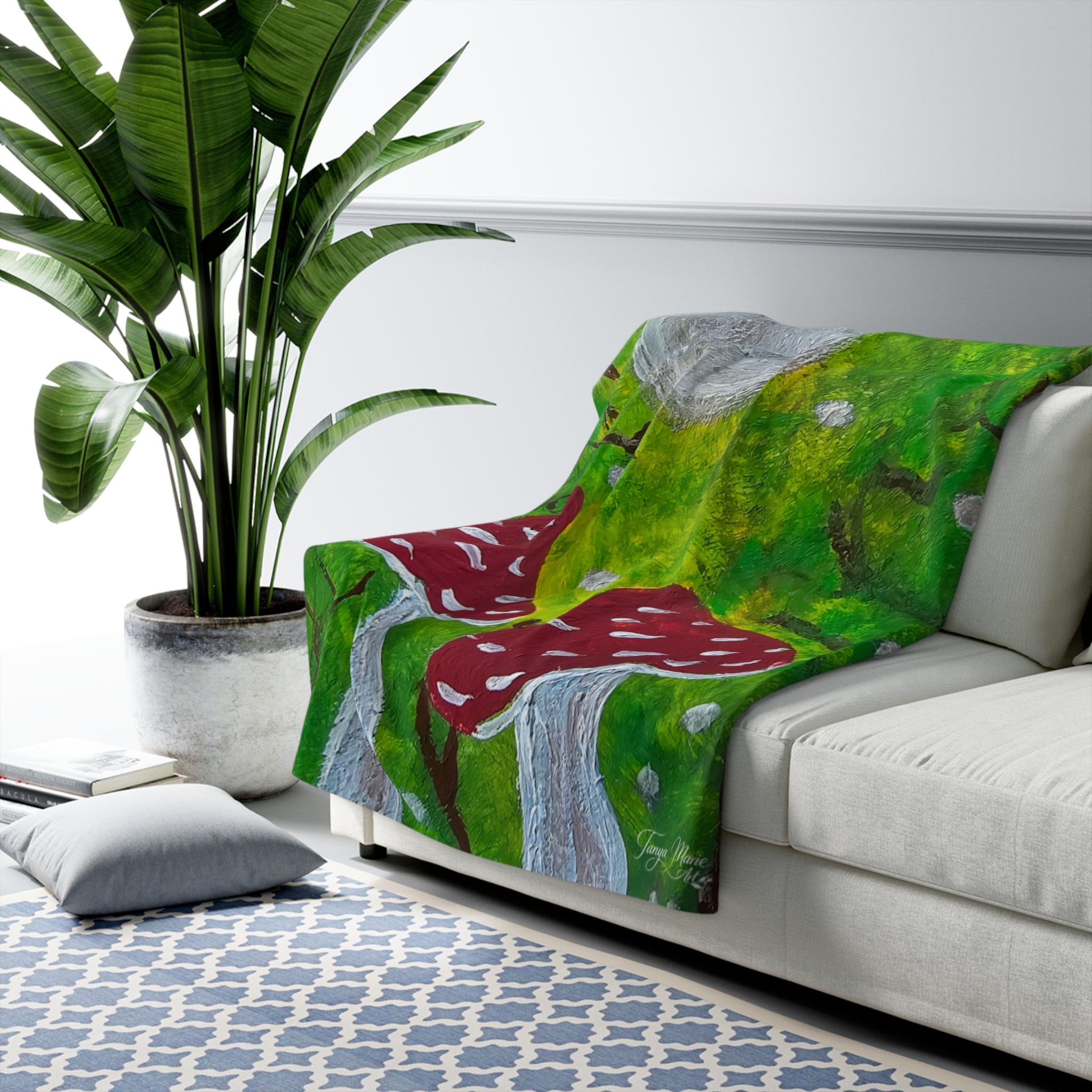 Sherpa blanket throw with green forest print, red mushrooms, and gray tree trunks, draped on sofa