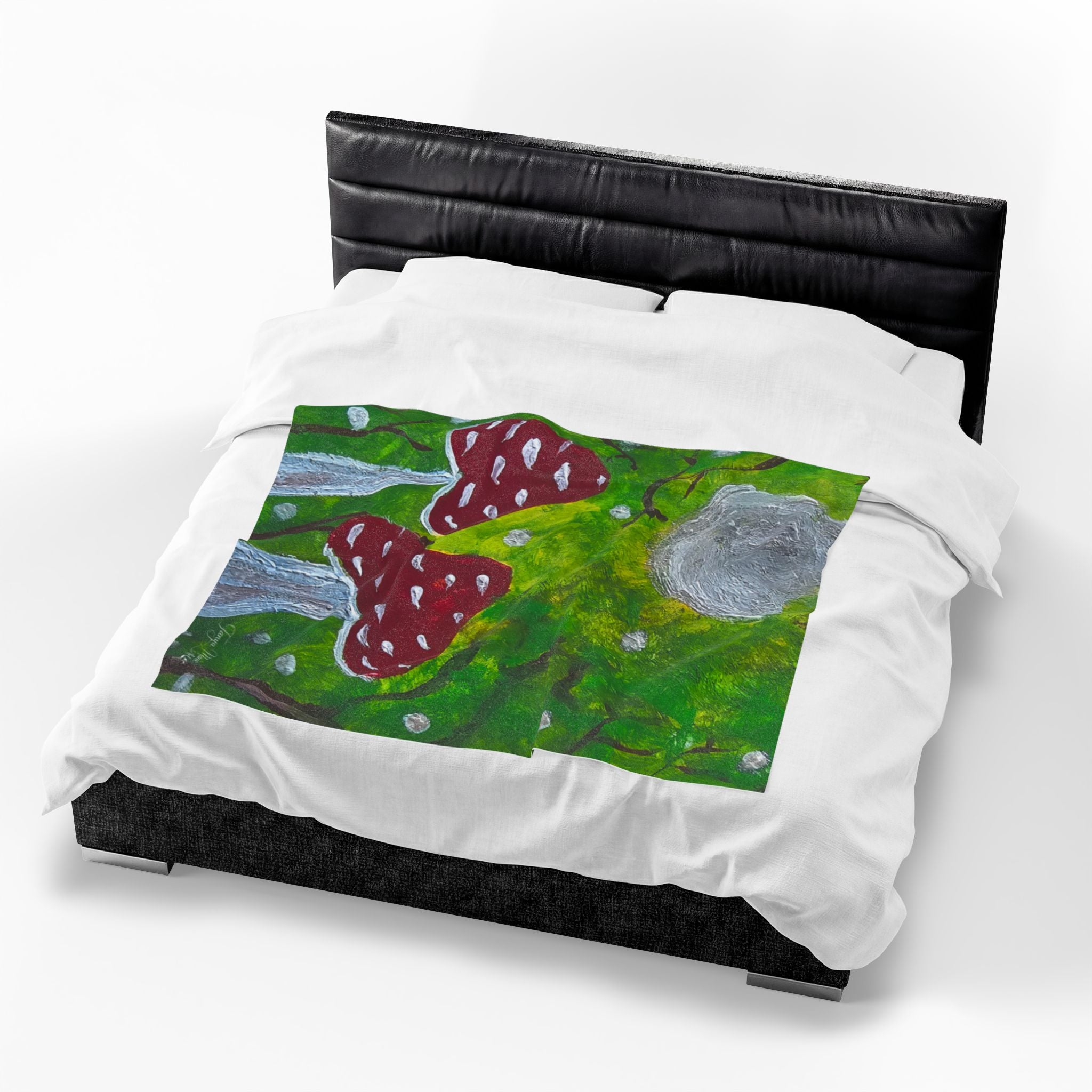 Plush velveteen blanket with green ground, red spotted mushrooms, and gray boulder
