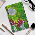 Spiral journal notebook with green forest cover, red mushrooms, gray moon, and black binding
