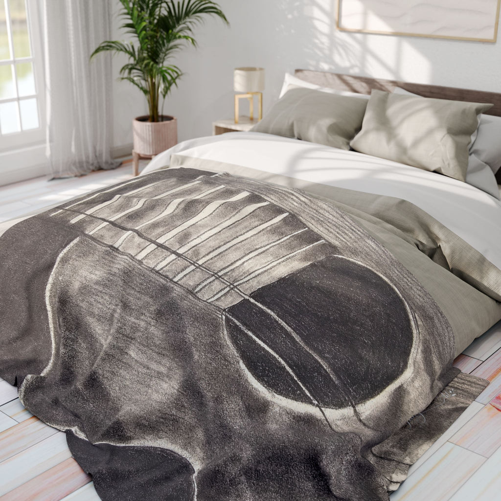 Gray fleece blanket on bed, acoustic guitar sketch centered