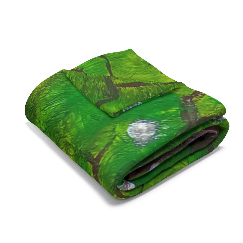 Folded green fleece blanket with gray moon and red mushroom graphic on top