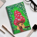 Spiral-bound fairy tale notebook with red mushroom house cover illustration on green