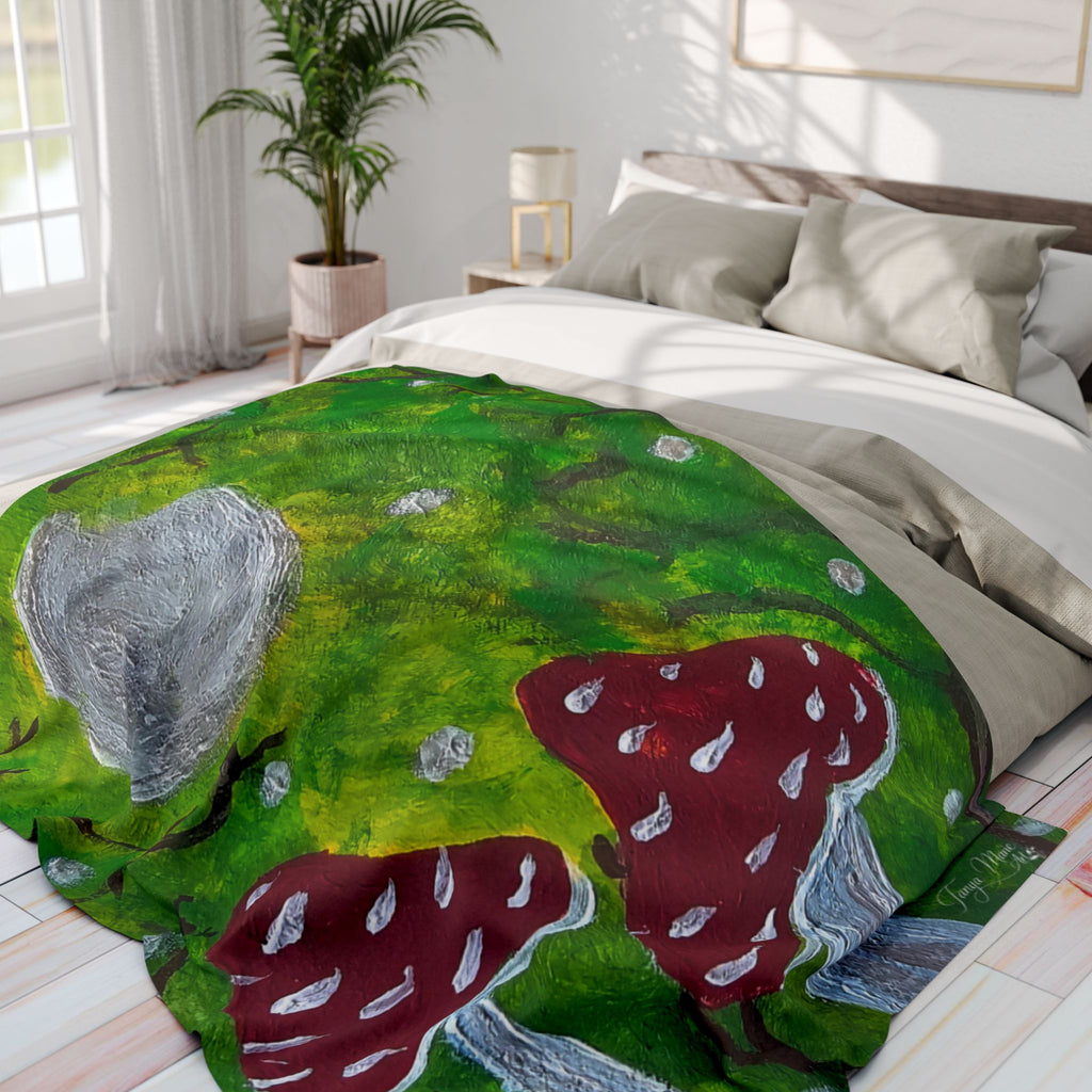 Green fleece blanket on bed corner, featuring red mushrooms and gray cap artwork