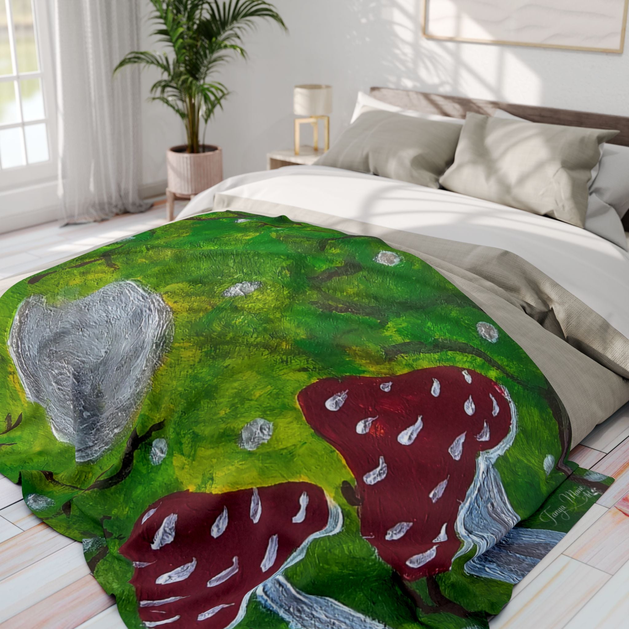 Green fleece blanket on bed corner, featuring red mushrooms and gray cap artwork