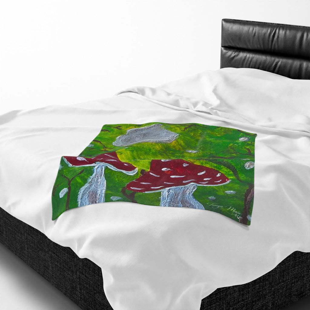 White plush blanket with green artwork panel showing red mushroom caps and gray moon.