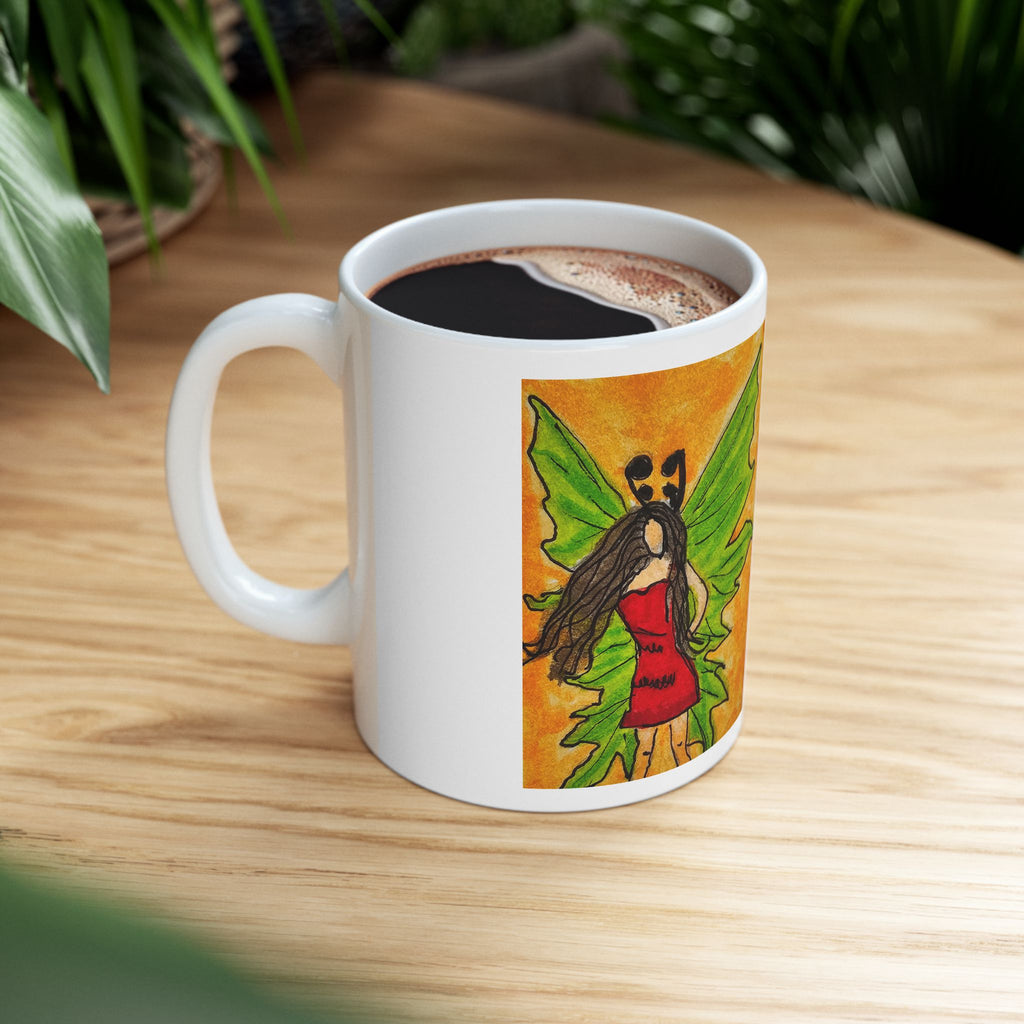 White ceramic mug on a wooden table with hot drink inside and a green-winged fairy print on front.