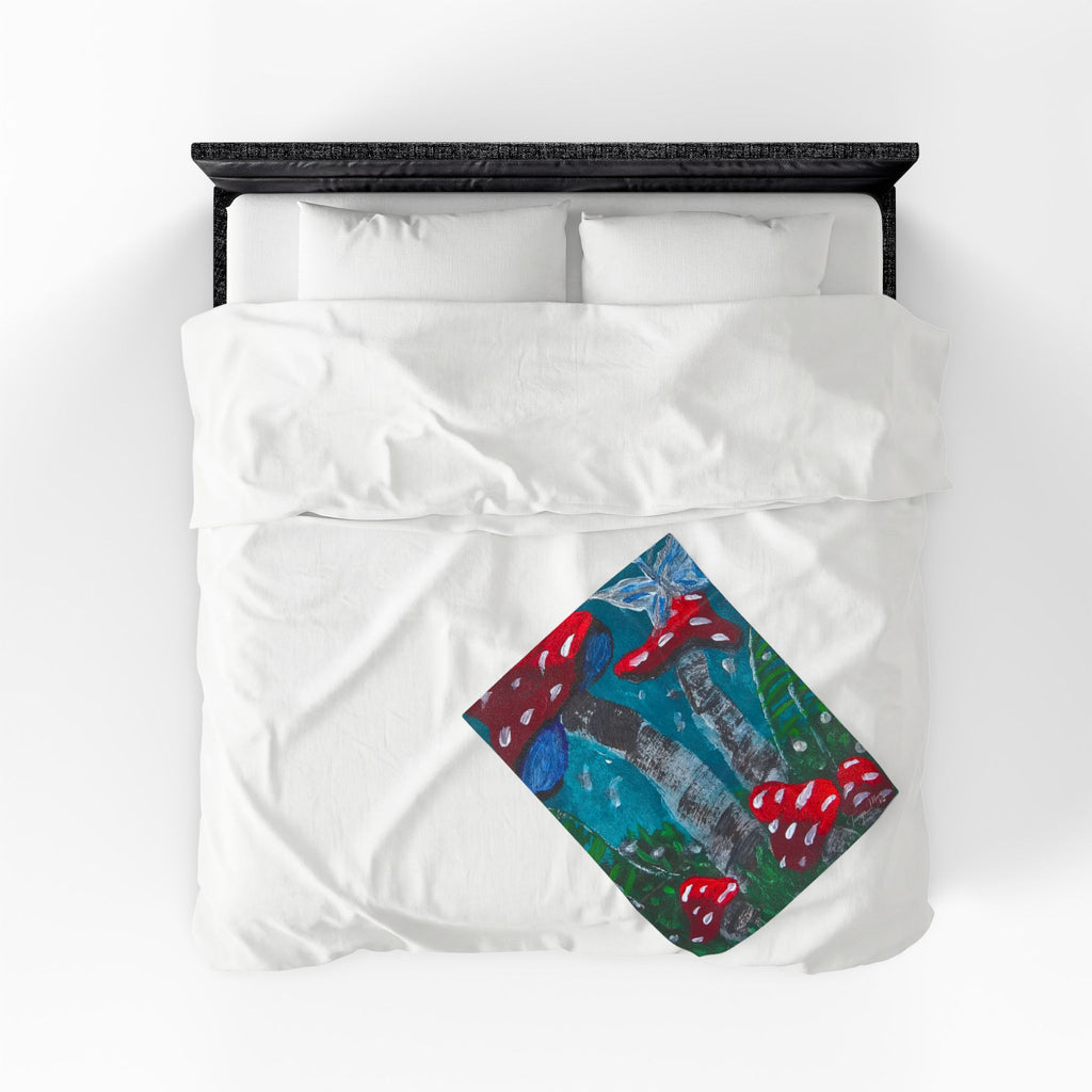 White plush throw blanket folded on bed with centered mushroom print square