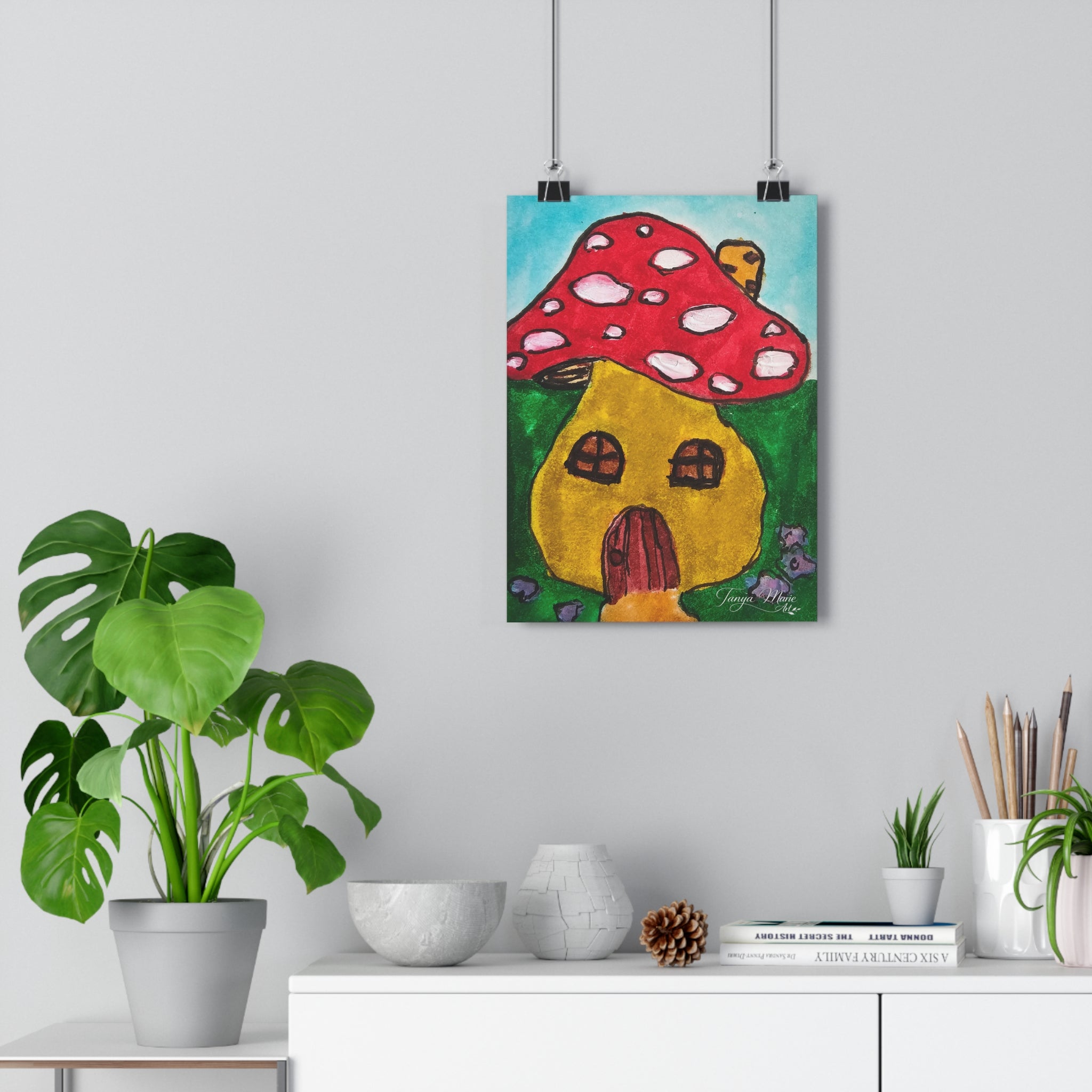 Mushroom cottage art print with red polka-dot cap and yellow house, hanging on wall