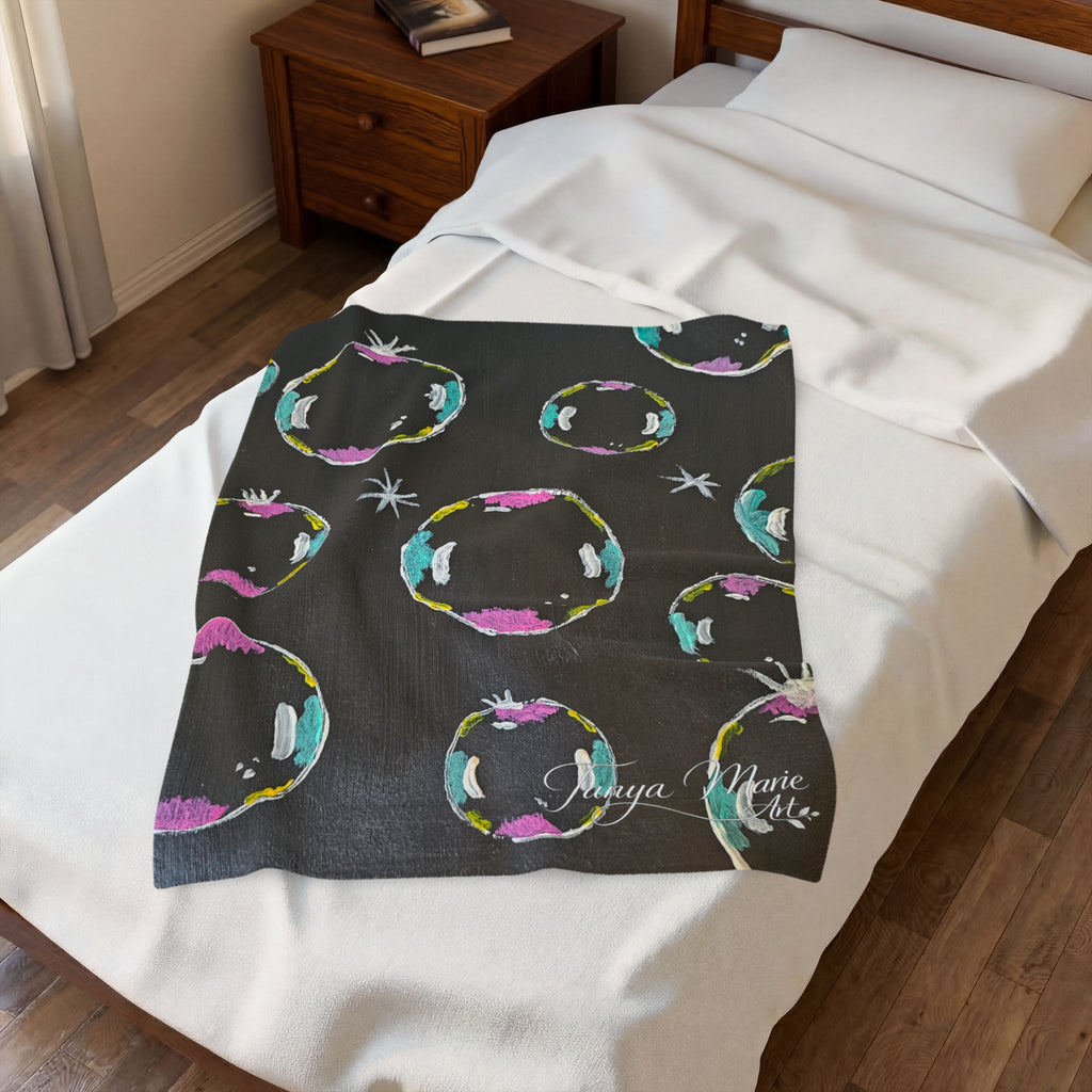 Plush blanket throw draped on bed, dark with colorful bubble ring motifs